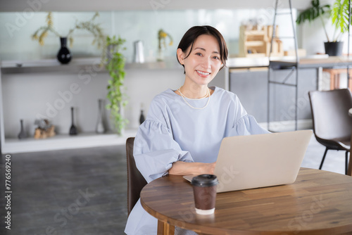 綺麗なオフィスやカフェでパソコンで仕事をする笑顔の美人なアジア系(日本人）女性の全身の広角のビジネスシーン カメラ目線