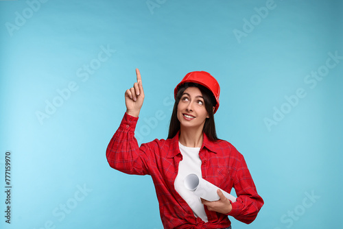 Architect in hard hat with draft pointing at something on light blue background