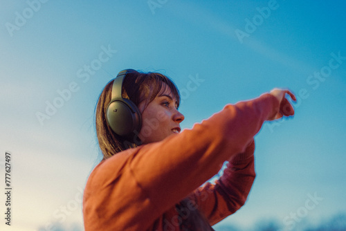 Young woman wears headphones and dances to music at sunset.