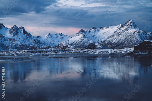Sea covered with ice surrounded by snowy mountains at sundown