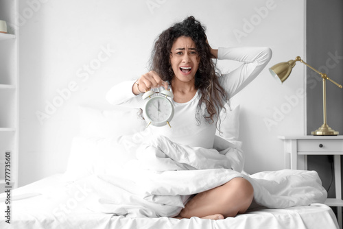 Overslept young African-American woman with alarm clock in bedroom