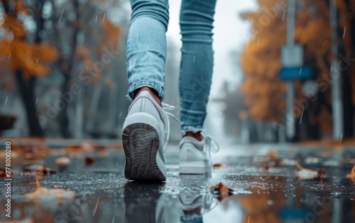 A person is walking down a street in the rain, wearing white sneakers and blue jeans. Concept of solitude and introspection, as the person is alone in the rain and he is lost in thought