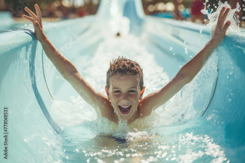 Happy boy going down the water slide in the water park, joyful children having fun splashing into pool