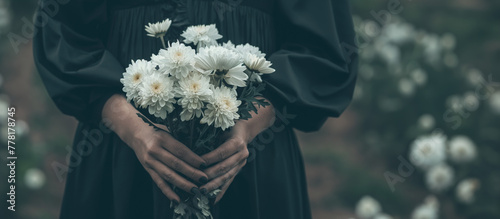 喪服を着て白い菊の花を手に持つ女性の手元のクローズアップ写真