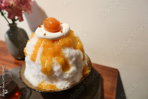 traditional Japanese sobert cold shaved ice dessert kakigori bingsu topped with orange marmalade sauce and fruit, oolong tea sauce on a black plate with white background and wooden table in summer