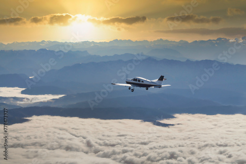 Kleinflugzeug fliegt über einer Wolkendecke in einen epischen Sonnenuntergang hinter einer Berglandschaft