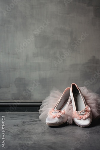 A pair of ballerina shoes with pale pink tulle on the top, resting against a grey wall with copy space.