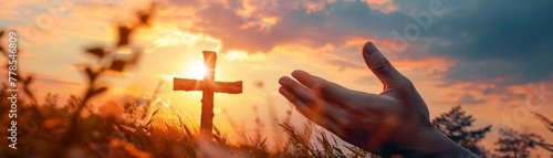 A hand reaches out towards a Christian cross in a symbolic gesture of faith and hope against a beautiful sunset backdrop.