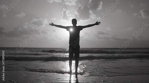 A man stands with his arms outstretched on the beach sunset, silhouette style, monotone black-white