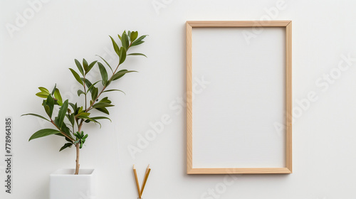 Minimalist composition with a wooden picture frame, green potted plant, and two pencils on a clean white background, leaving copy space.