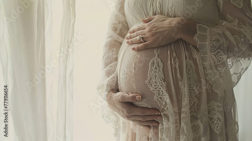 Closeup of a pregnant woman's belly, with her hands holding her stomach against a white room background, 