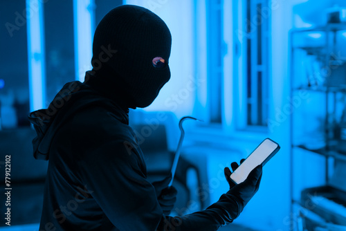 Thief using a smartphone during a break-in