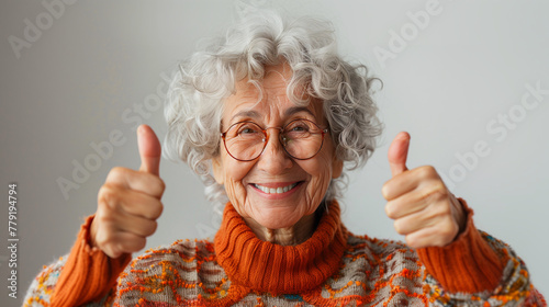 Femme joyeuse levant les pouces en l'air, photographie sur fond blanc, grand-mère de 70 ans avec des lunettes et un col roulé