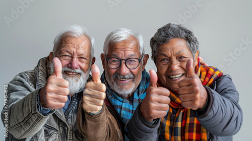 Groupe de trois amis âgés, 60 à 70 ans, levant le pouce vers le ciel, fond blanc, sortie entre seniors