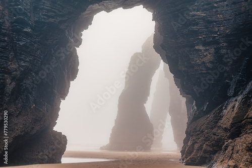 Playa de Las Catedrales in foggy day. Catedrais beach in Ribadeo, Lugo, Galicia, Spain. Natural archs of Cathedrals beach. Moody rock formations on misty day. Travel destination