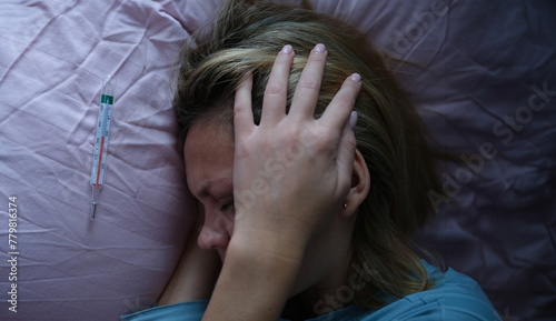 Young woman in bed and holding her head near mercury thermometer. Symptoms of bacterial meningitis concept