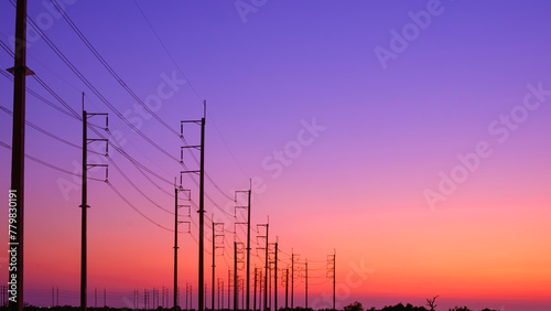 Silhouette two rows of electric poles with cable lines on curve country road against colorful twilight sky background after sundown