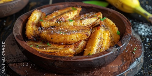 A bowl of fried bananas with a sprinkle of salt on top. The bowl is on a wooden table