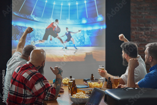 Men, friends sitting at table with beer and snacks, watching online basketball game translation on TV and cheering up favorite team. Concept of sport, championship, game, sport fans, leisure