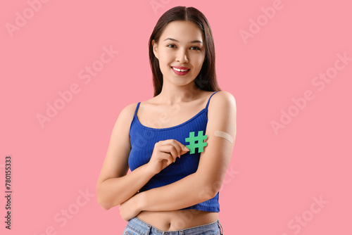 Beautiful young woman with applied medical patch holding hashtag sign on pink background