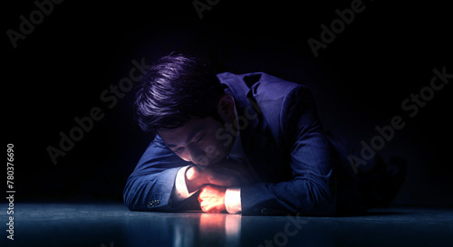 失敗し暗い部屋で跪き項垂れ絶望するスーツを着た仕事中のビジネスマンの日本人男性 後悔・謝罪・増税・落ち込む・鬱・破産のイメージ