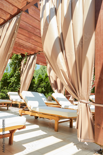 A serene setting at a luxury resort featuring a row of elegant cabanas with flowing drapes and comfortable sun loungers, bathed in warm sunlight, inviting guests to relax and enjoy a peaceful day.