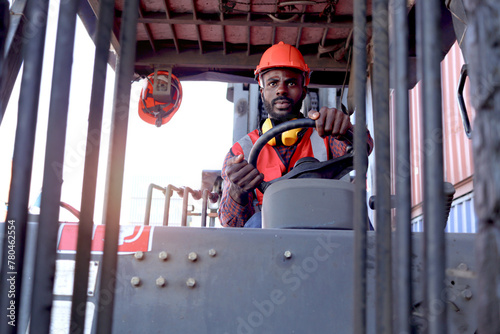 Industrial worker man wearing safety bright neon red vest and helmet driving forklift car at plant factory industry, African American engineer male working at logistic shipping cargo container yard.