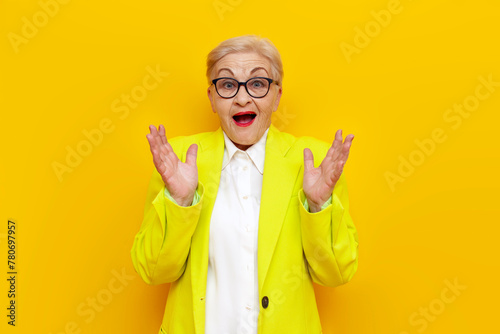 surprised old businesswoman in glasses and formal wear looks away in shock on yellow isolated background, elderly pensioner grandmother in blazer worries in amazement