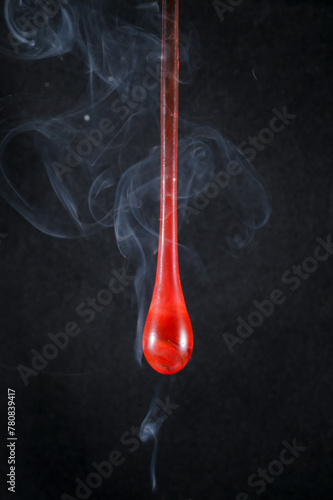 Gota de vidro vermelho semi transparente em fundo preto. Fotografia em close up de uma peça similar a um líquido de alta viscosidade pingando.