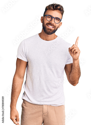 Young hispanic man wearing casual clothes and glasses pointing finger up with successful idea. exited and happy. number one.