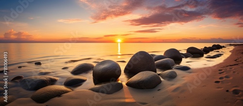 Golden hour casts warm hues on a serene coast with smooth rocks and gentle waves under the pink sky