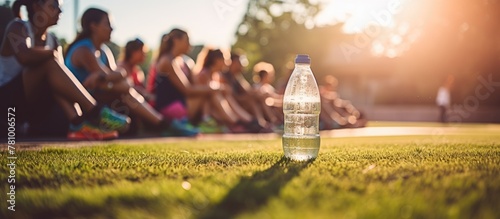 Several people gathered outdoors on the green lawn with a clear bottle of water placed in front of them