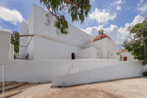 The exterior of Puig de Missa church in Santa Eulalia, Ibiza, captures the essence of Mediterranean architecture with its stark white walls and distinctive terracotta dome amidst lush greenery