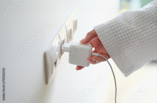 Woman hand in robe gown inserts white charger into socket in hotel rooms or at home. Charge gadgets correctly concept