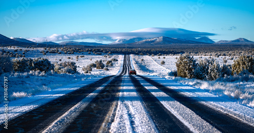 Frozen highway from Grand Canyon National Park to Williams Arizona on a cold sunny winter morning. Snow covered lanes in wide american landscape with oncoming truck. Symmetric panorama of wide scenery