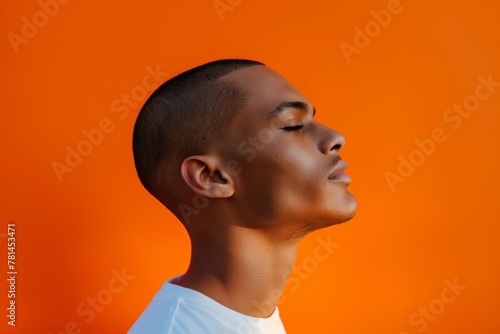 Side profile of a young man displaying his fresh buzz haircut with a vibrant orange backdrop