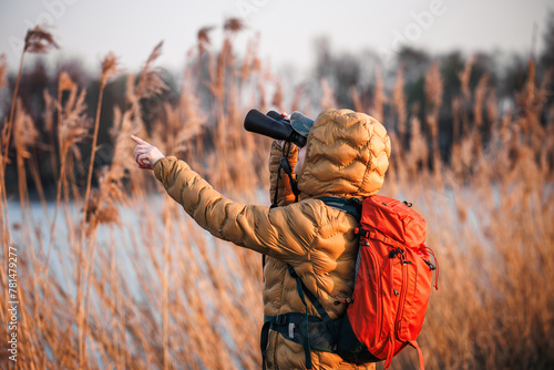 Woman naturalist with binoculars is looking for animals and birds at lake. Bird watching and wildlife observation. Eco tourism