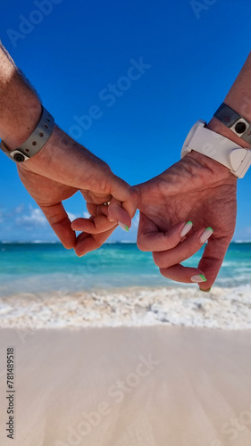 dwoje ludzi na plaży trzyma się za ręce, w oddali morze, słońce, fale