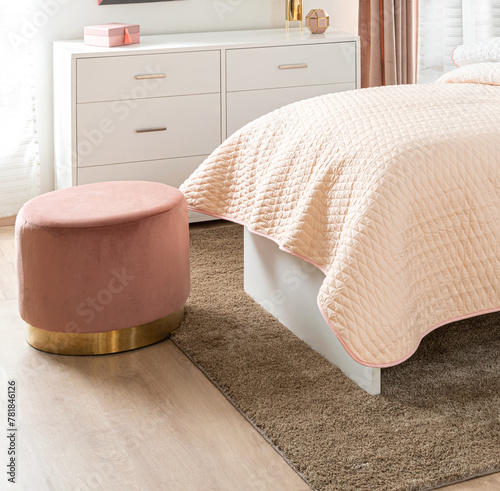 Elegant Feminine Bedroom Interior in Soft Pink Hues Featuring Plush Bedding, a Round Velvet Ottoman with Golden Base, a White Minimalist Dresser, Coordinated Textiles, Emphasizing Comfort and Style.