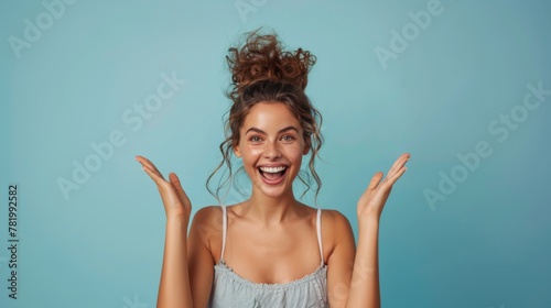 Excited young woman with a joyful expression raising her hands in surprise on a turquoise background.