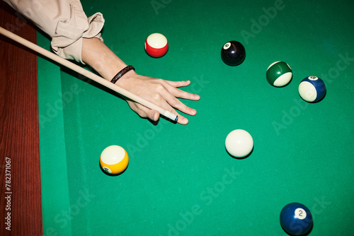 Top view closeup of male hand holding cue stick and playing billiard at green pool table with camera flash copy space