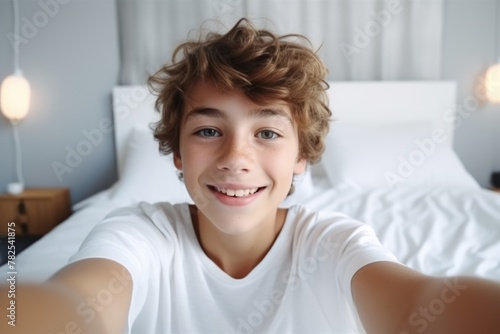 A smiling young teen captures a self-portrait with a camera in a bright, cozy bedroom setting. Happy Teenager Taking Selfie in Bedroom