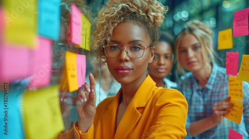 Business womans pointing on glass with colorful paper notes. Diverse group of female employees in formal wear using stickers. 