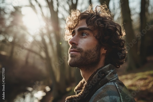Portrait of a handsome young man with curly hair looking away in the forest