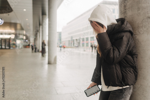 Upset and depressed girl holding smartphone and holding head. University sad student suffering from depression at high school. Lonely bullied teen