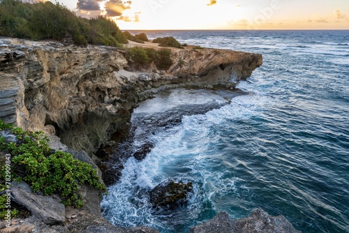 The sun slowly rises over jagged cliffs, meeting the rough turquoise waters of the Pacific Ocean along the Mahaulepu Heritage Trail in Koloa, Hawaii on the island of Kauai.