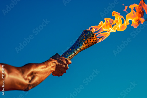 A close-up of an athlete's hand holding the olympic torch stands solemnly against the blue sky. space for copying.