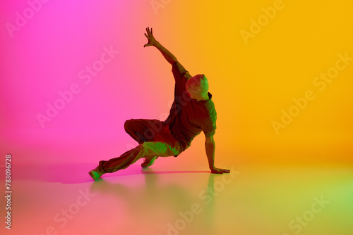 Young man, dressed streetwear performing freestyle moves in motion in neon light against gradient pink-yellow background. Concept of art, hobby, sport, creativity, fashion and style, action. Ad