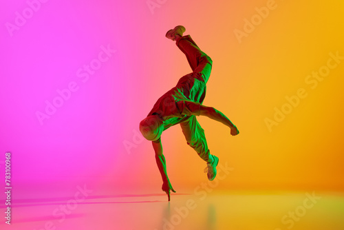 Dynamic photo of young, talented man dancing in freestyle in neon light against gradient pink-yellow background. Concept of art, hobby, sport, creativity, fashion and style, action. Ad