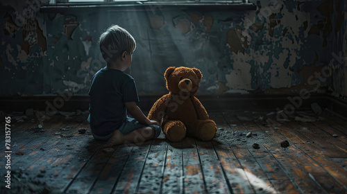 Young boy and his teddy bear are sitting on the floor of a dark